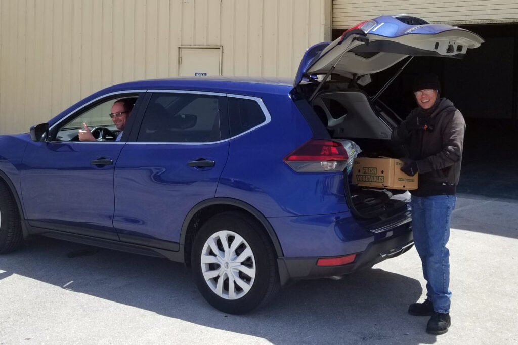 employee loading produce box into trunk of a customer's car
